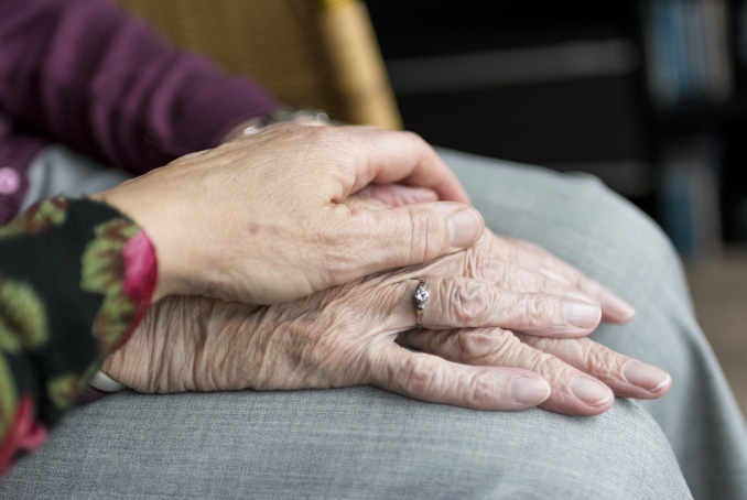 Photo de mains d'une personne âgée en gros plan, avec la main d'une personne aidante posée dessus